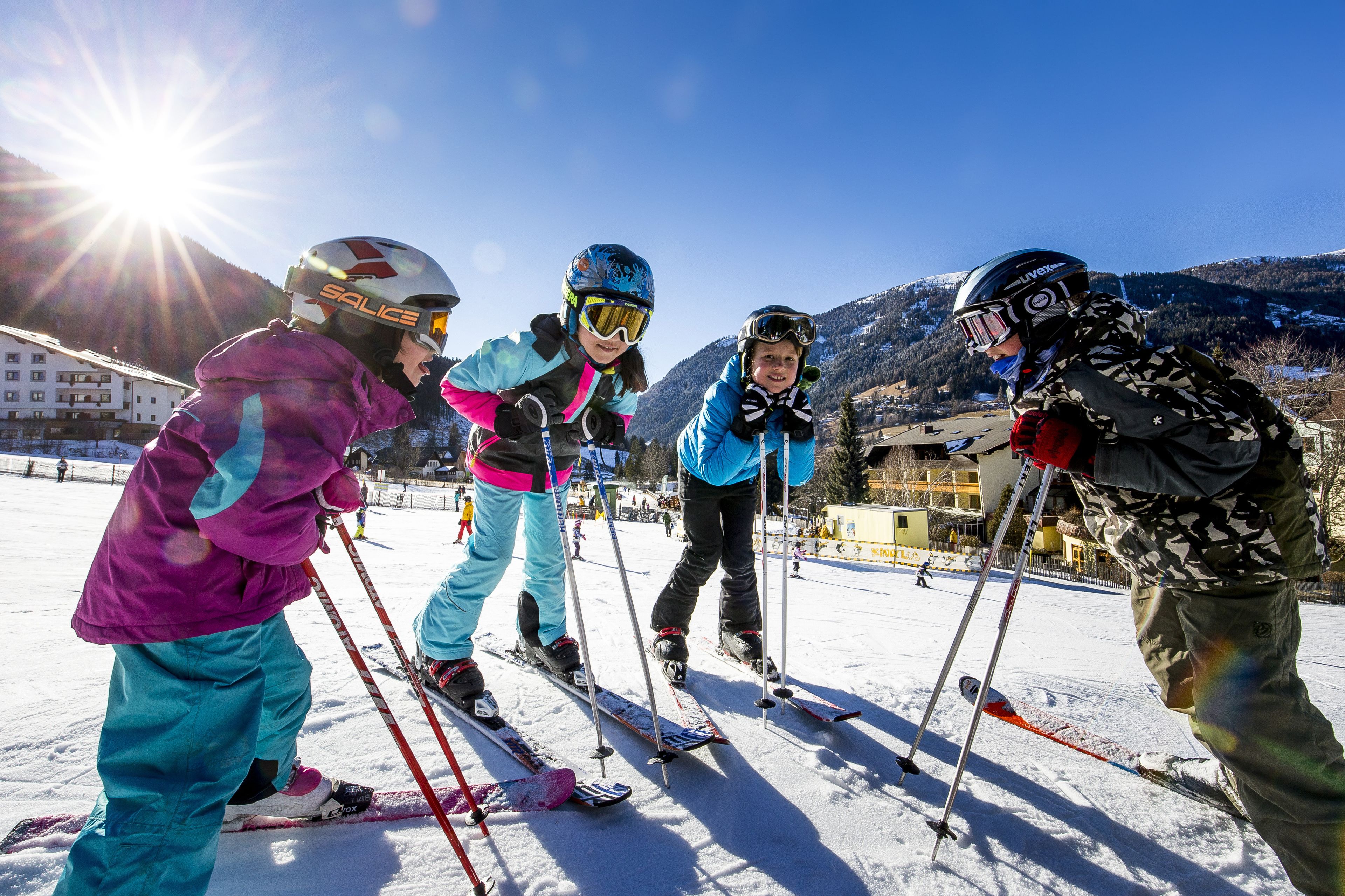 A group of skiers on a snowy slope with a clear sky and mountains in the background.