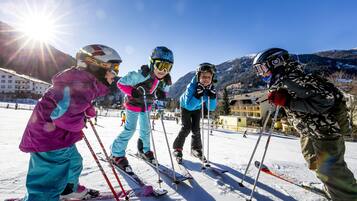 A group of skiers on a snowy slope with a clear sky and mountains in the background.