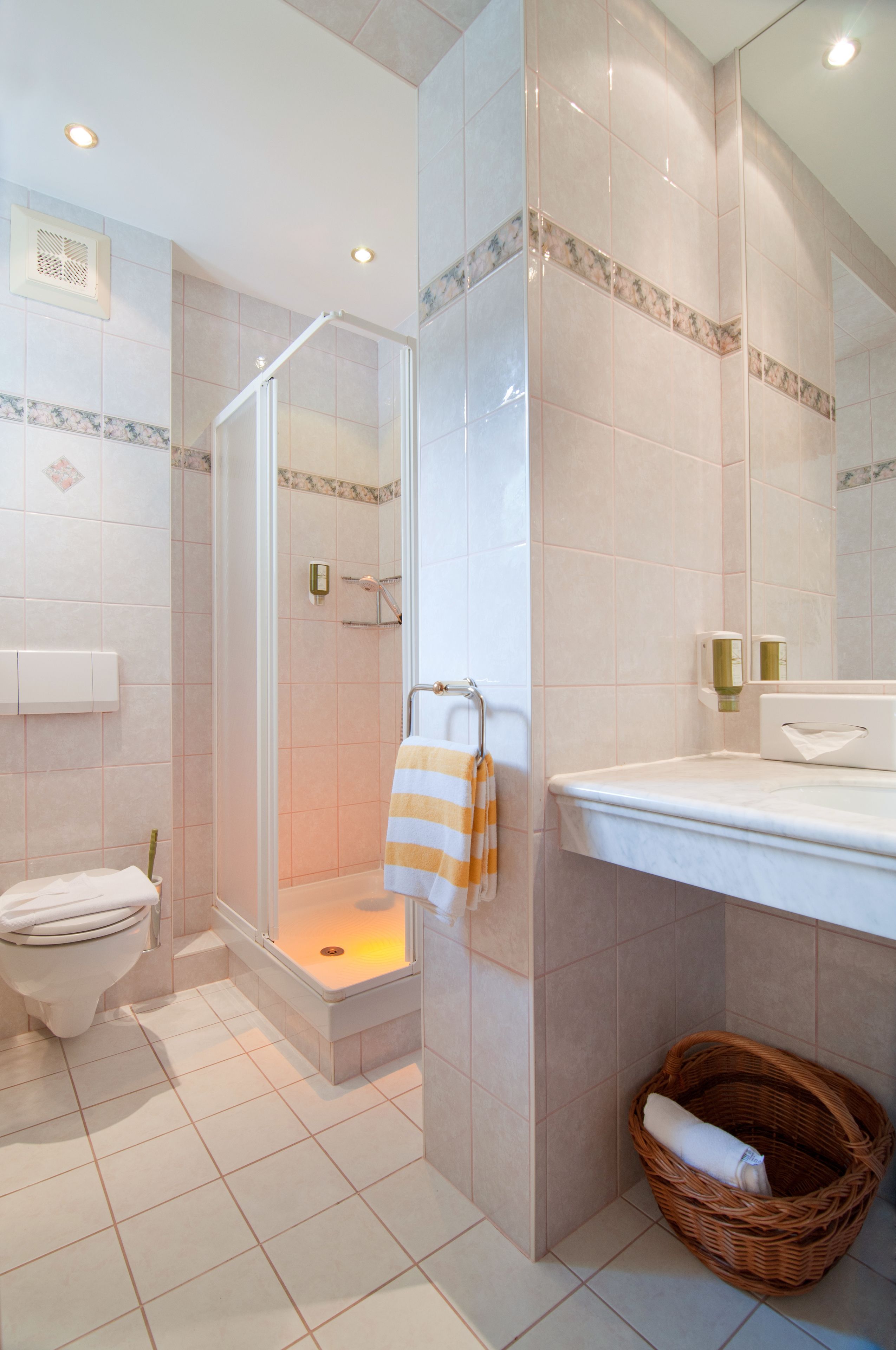 A bathroom with a toilet, a shower with a glass door, a sink, a mirror, and a wicker basket.