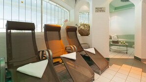 Een wellnessruimte met ligstoelen, een massagetafel en uitzicht op het buitenlandschap door grote ramen.