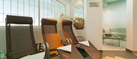 A spa area with reclining chairs, a massage table, and a view of the outside through large windows.