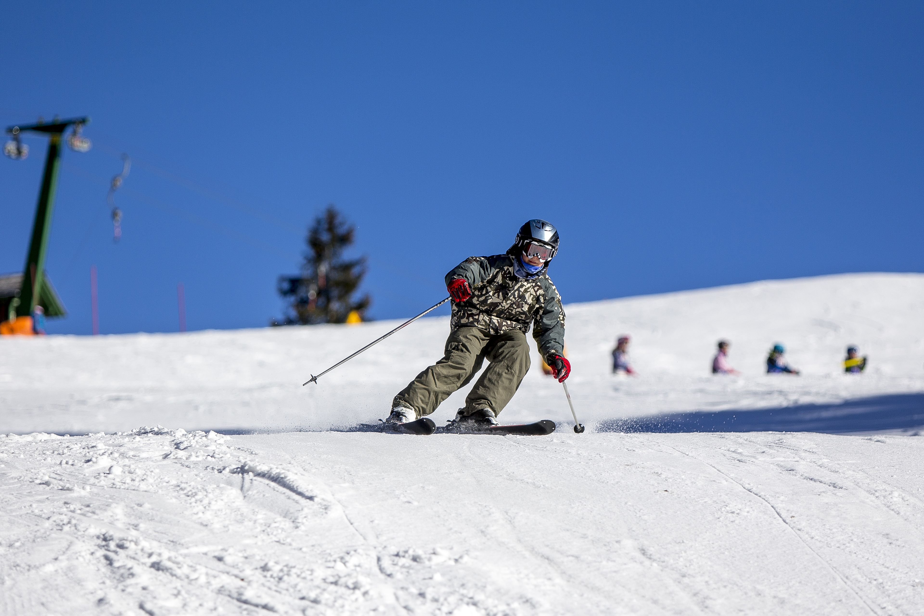 A skier on a snowy slope with a clear blue sky.