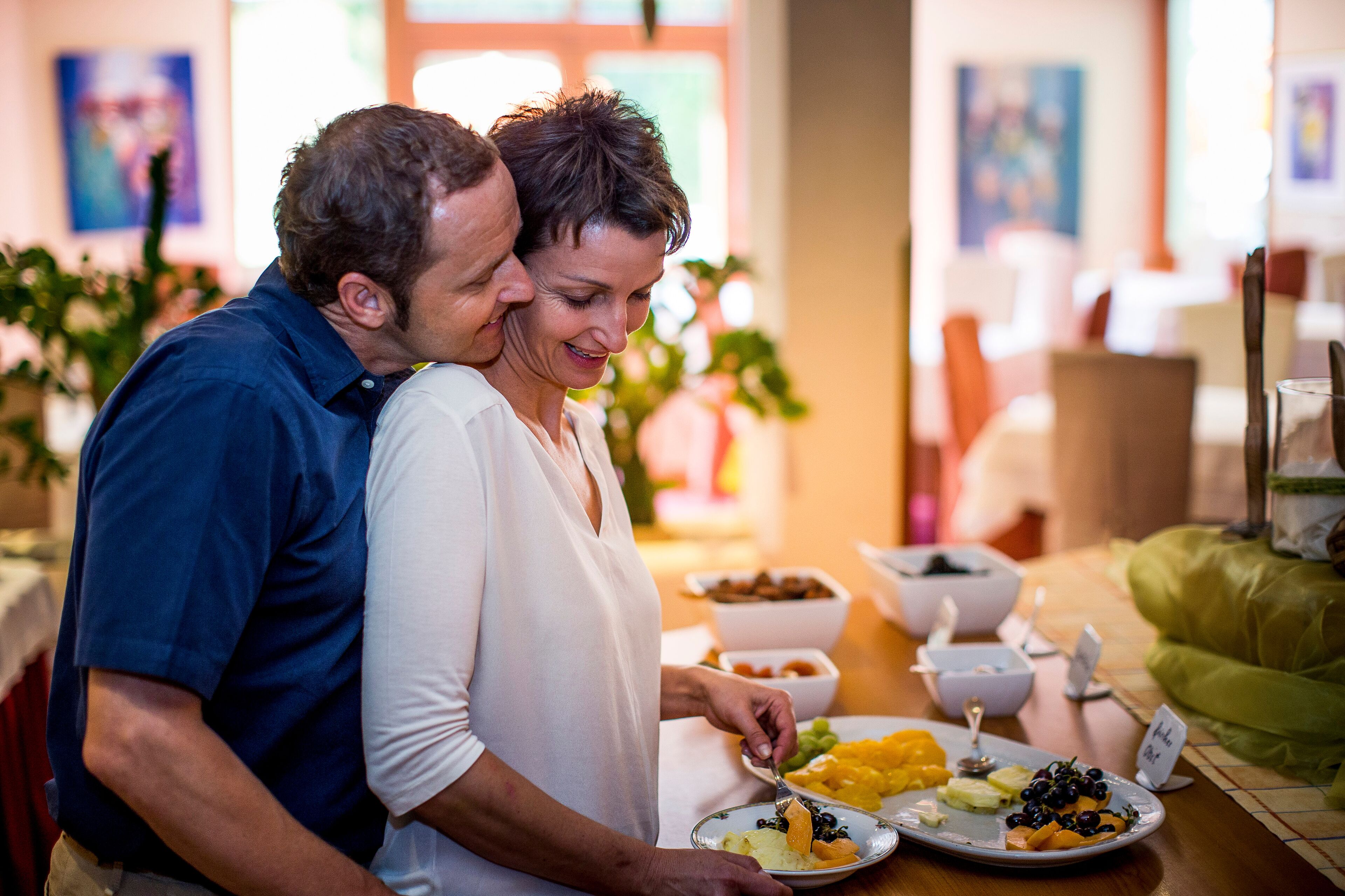 A couple dining at a table with various dishes, including fruits and a bowl of nuts.