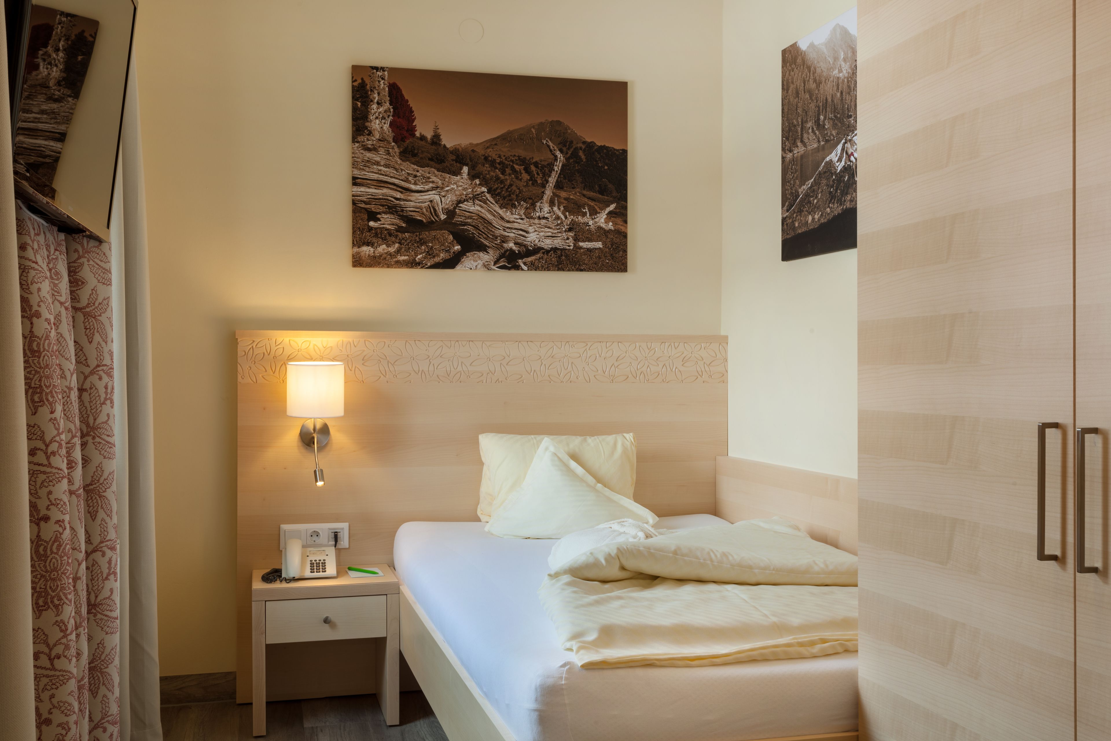 Una habitación de hotel con cama, mesita de noche, lámpara y dos cuadros en la pared.