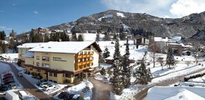 A hotel with a snow-covered roof, multiple balconies, and a view of a snowy mountain. - Family & Sporthotel Kärntnerhof (Bad Kleinkirchheim)