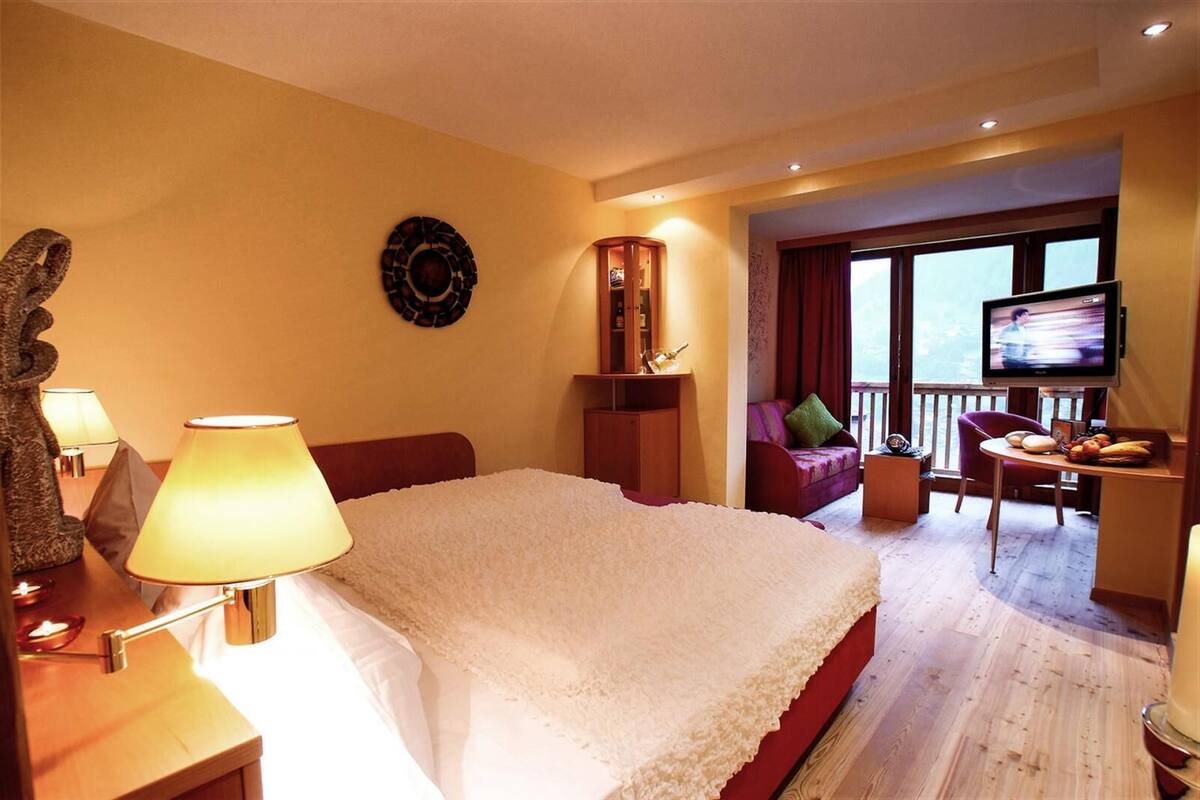 Habitación de hotel con una cama grande, un escritorio con lámpara, televisión y balcón con vistas.