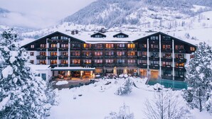 Een groot, meerhoog hotel met balkons en een zwembad, omringd door besneeuwde bergen.
