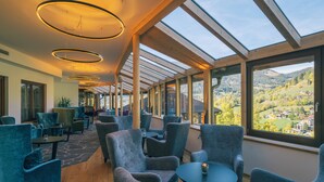 Een modern interieur met een lange rij blauwe fauteuils en tafels, grote ramen met uitzicht op een bergachtig landschap.