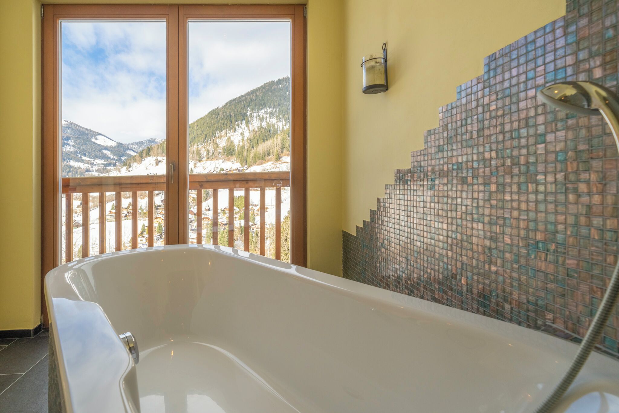 A bathroom with a freestanding bathtub, a glass shower enclosure, and a view of snow-covered mountains through a large sliding door.