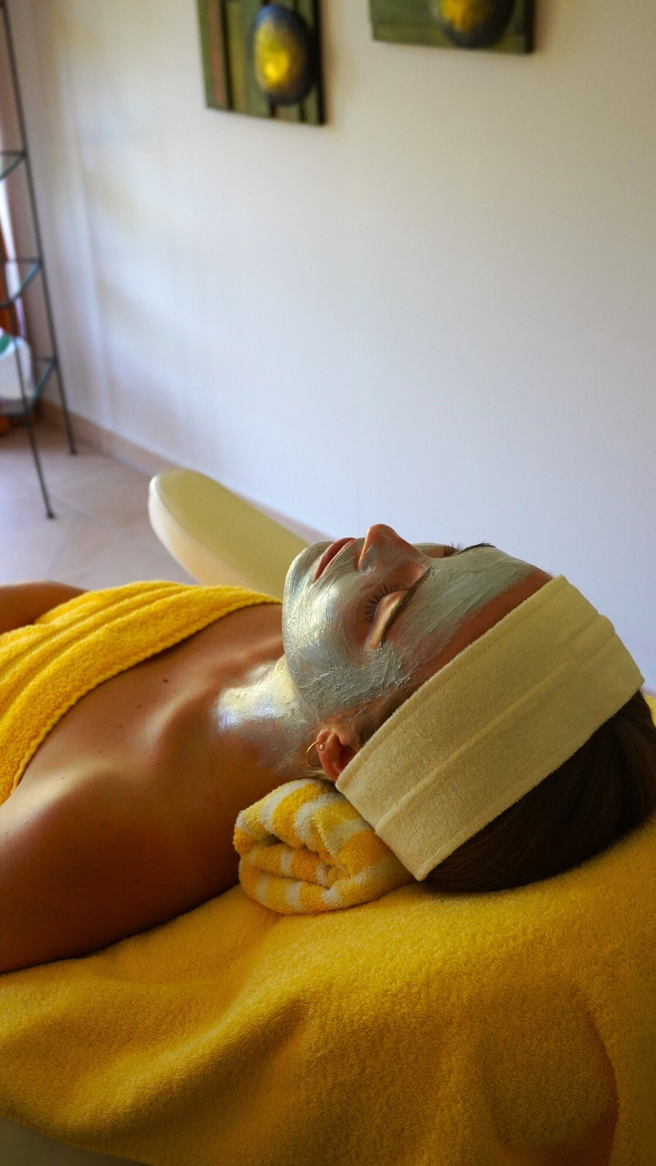 A person lying on a bed with a yellow towel, in a room with a white wall and a painting.