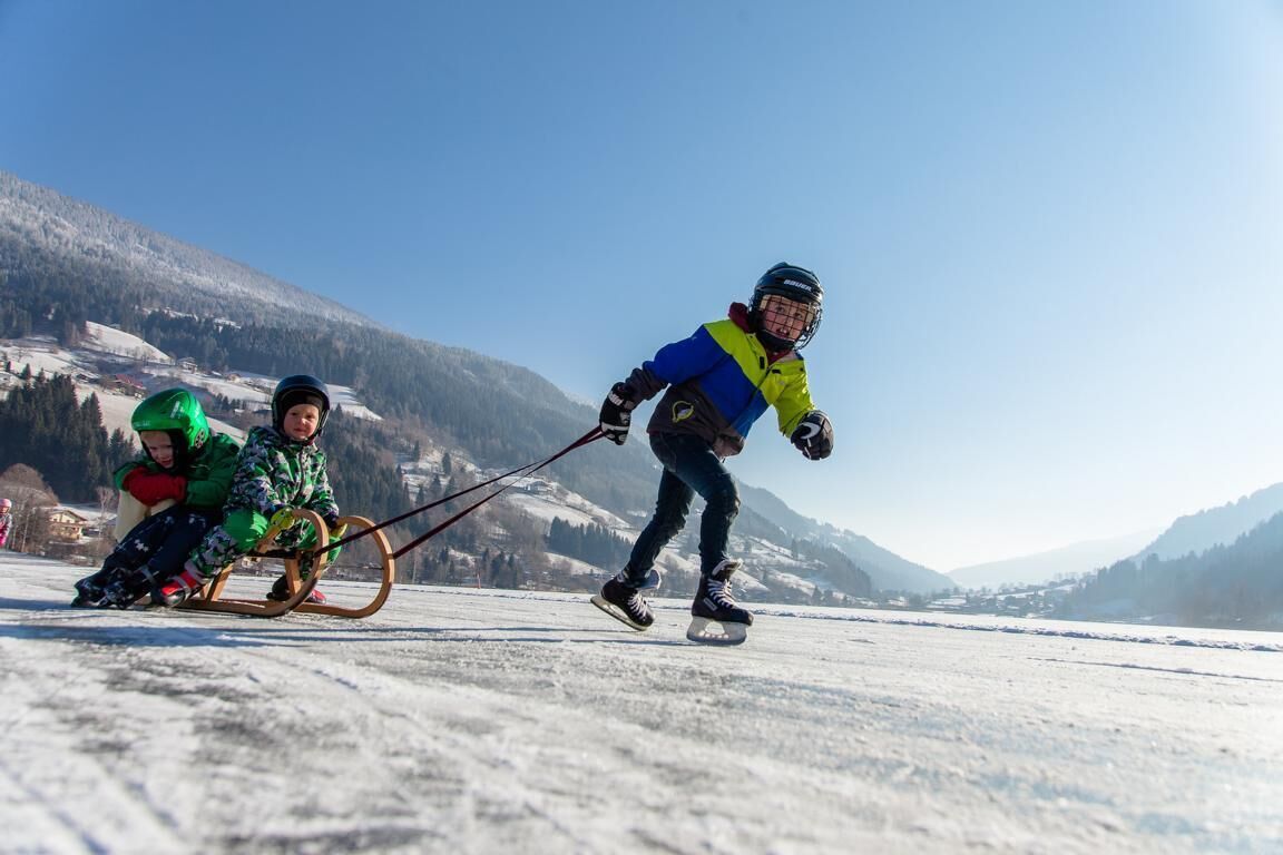 Drie kinderen sleeden op een besneeuwde helling, met een bergachtige achtergrond.