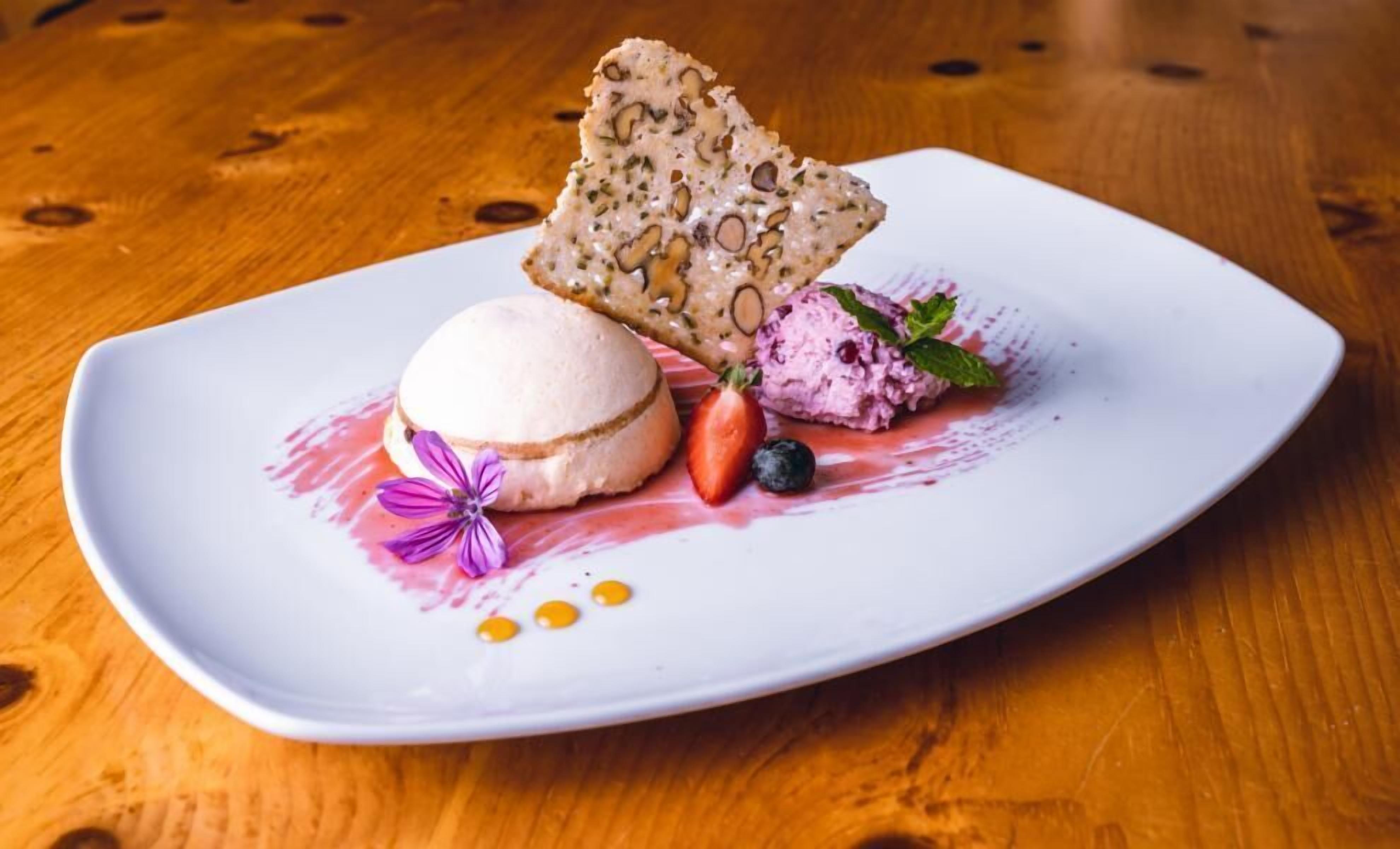 A dessert plate with a scoop of ice cream, a strawberry, a blueberry, and a piece of bread on a white plate.