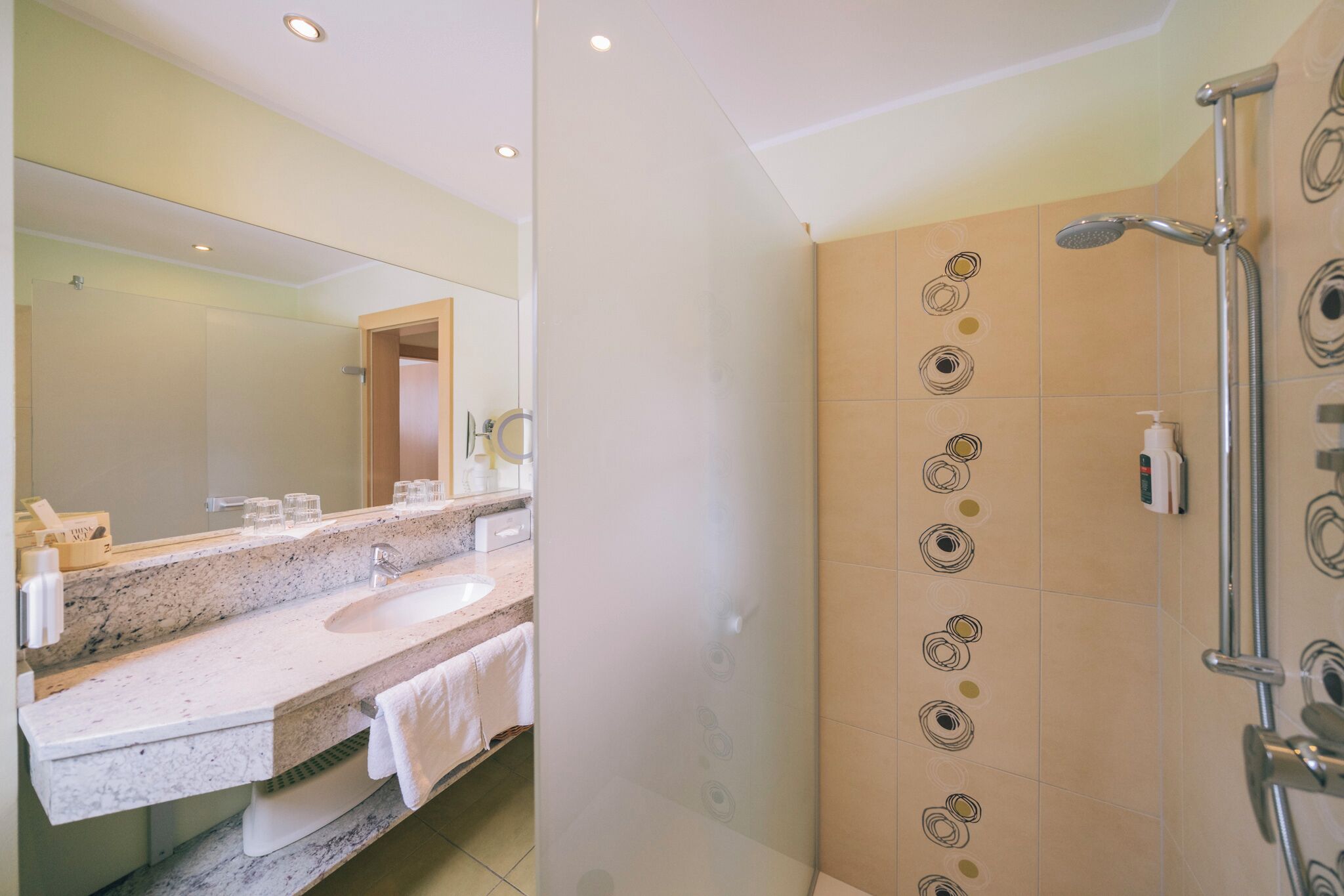A bathroom with a marble sink, a large mirror, and a shower with a control panel.