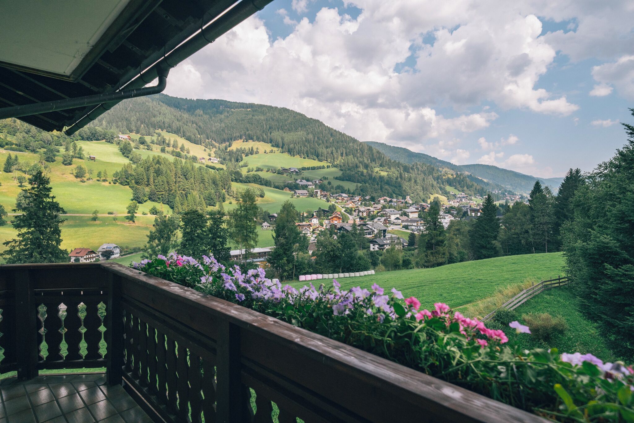 Ein Balkon mit Blick auf ein grünes Tal, Häuser und ein Gebirge.