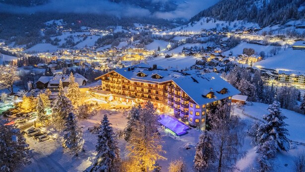 Een besneeuwde stad aan de voet van een berg 's nachts, met verlichte gebouwen en een opvallend hotel met meerdere verdiepingen en balkons.