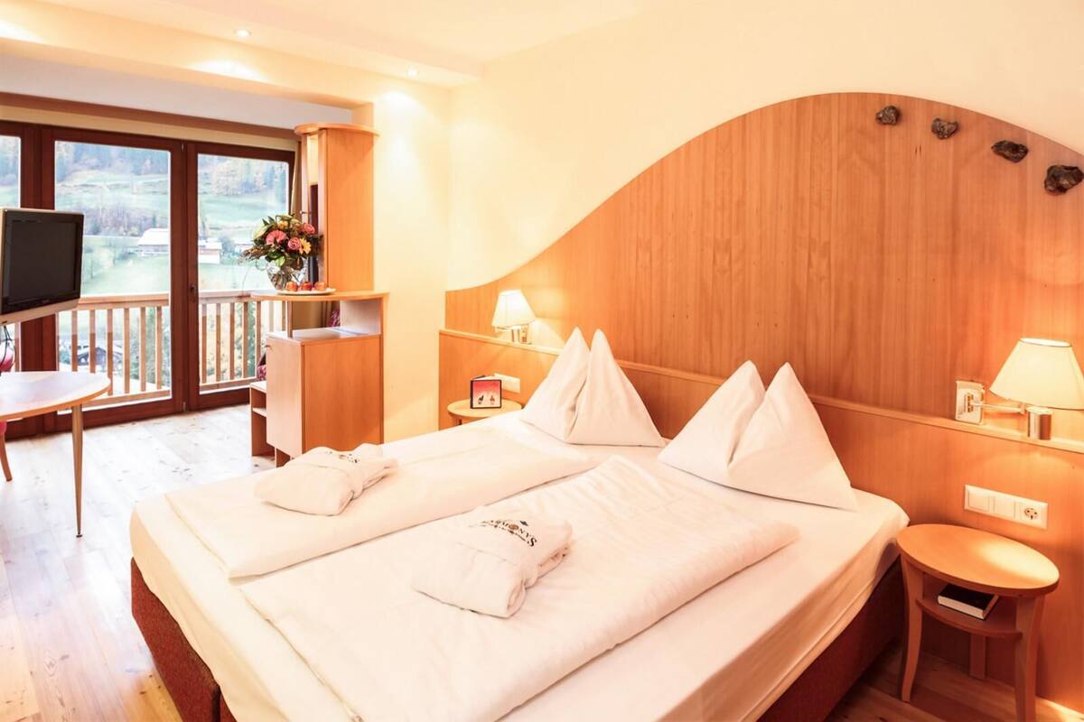 Habitación de hotel con una cama grande, un escritorio, un televisor y un balcón con vistas.