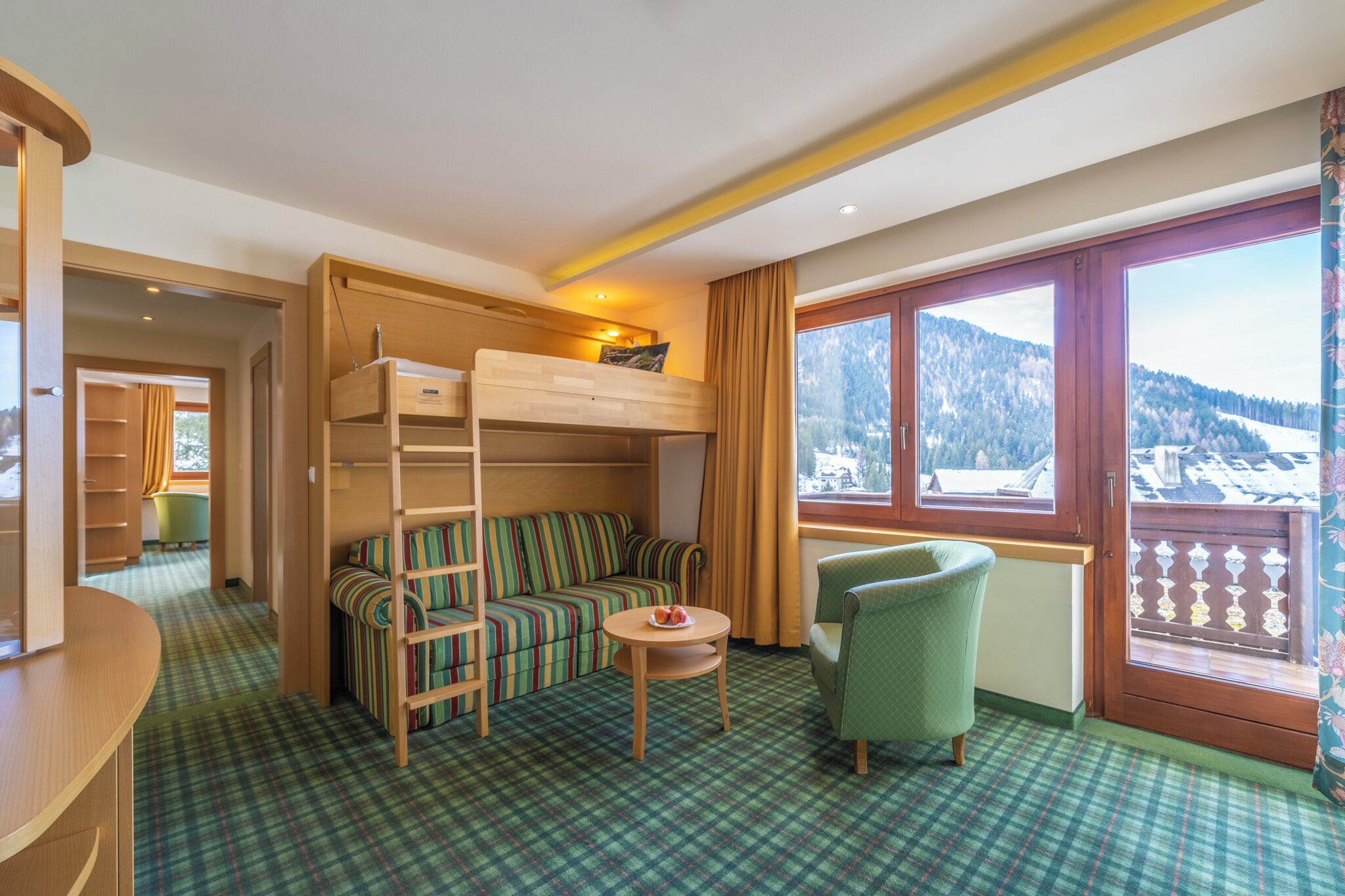 Ein Zimmer mit einem Etagenbett, einer Schlafcouch, einem kleinen Tisch und einem Stuhl. Ein Fenster bietet Blick auf eine verschneite Landschaft.