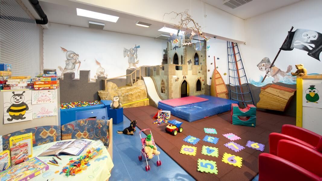 Una sala de juegos con una estructura tipo castillo, un tobogán y diversos juguetes y rompecabezas.