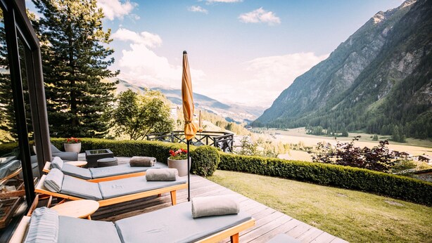 A deck with lounge chairs and a wooden table, overlooking a mountainous landscape. - Nationalpark Lodge Grossglockner (Heiligenblut)