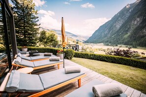Una terraza con sillones de descanso y una mesa de madera, con vista a un paisaje montañoso.