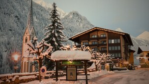 A snow-covered mountain scene with a church, a lodge, and a sign indicating a parking area. - Nationalpark Lodge Grossglockner (Heiligenblut)