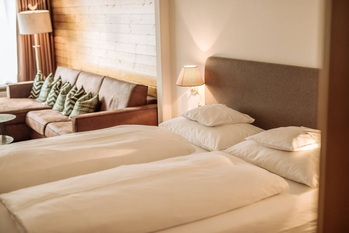 A hotel room with two beds, a sofa, and a lamp.