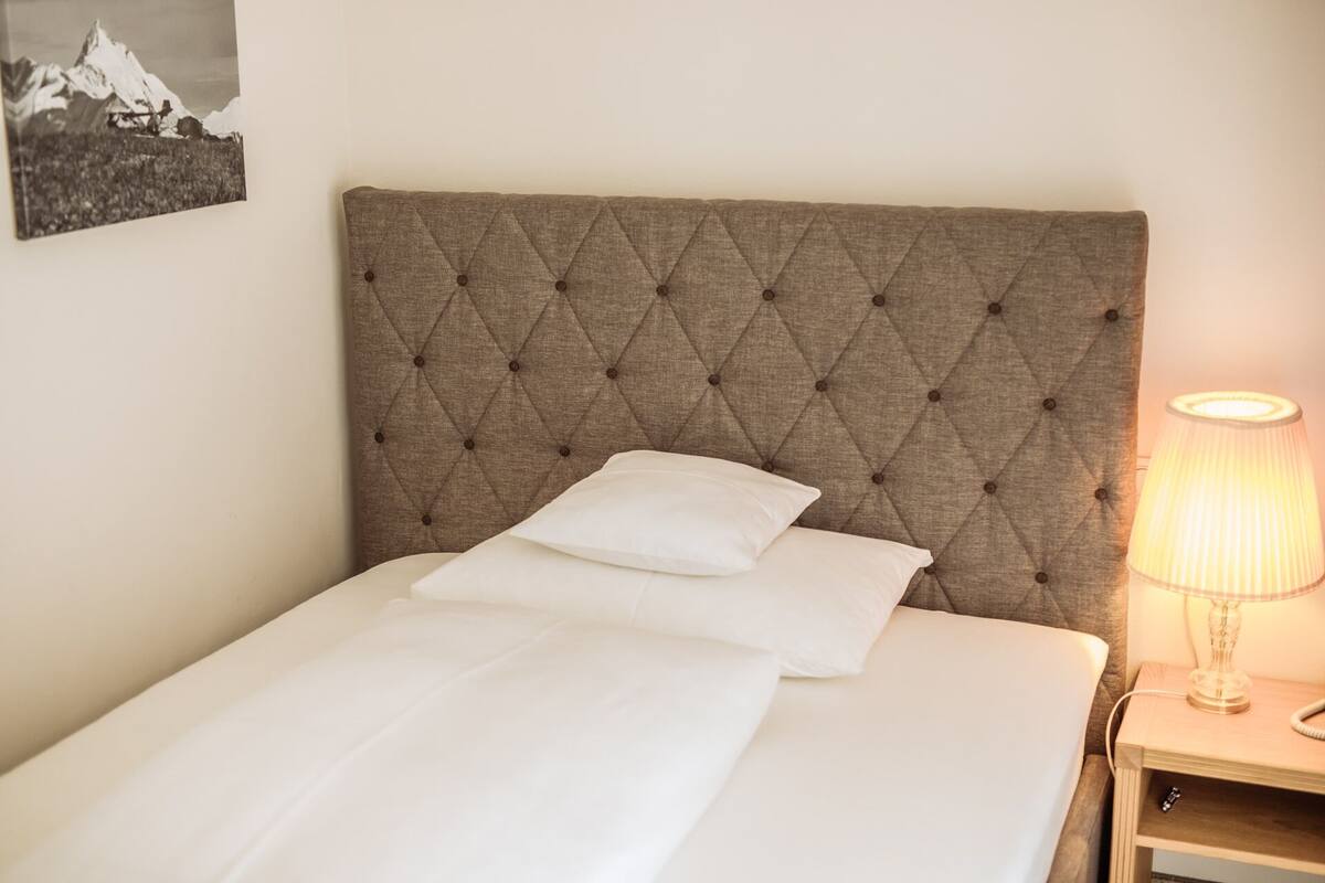 A neatly made bed with a tufted headboard, a bedside lamp, and a framed picture on the wall.