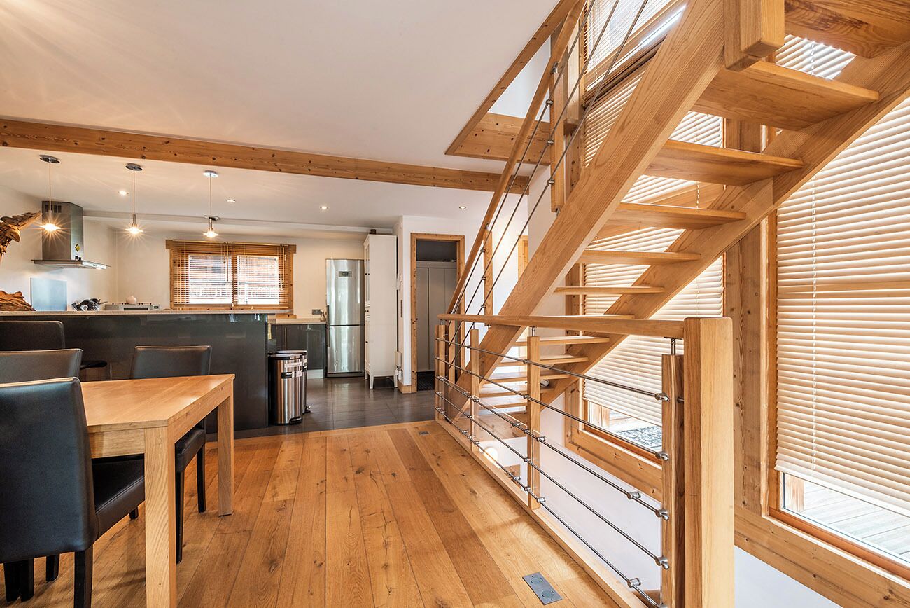 A spacious kitchen with wooden flooring, a dining area with chairs, and a staircase with wooden railings.