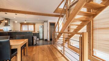 A spacious kitchen with wooden flooring, a dining area with chairs, and a staircase with wooden railings.