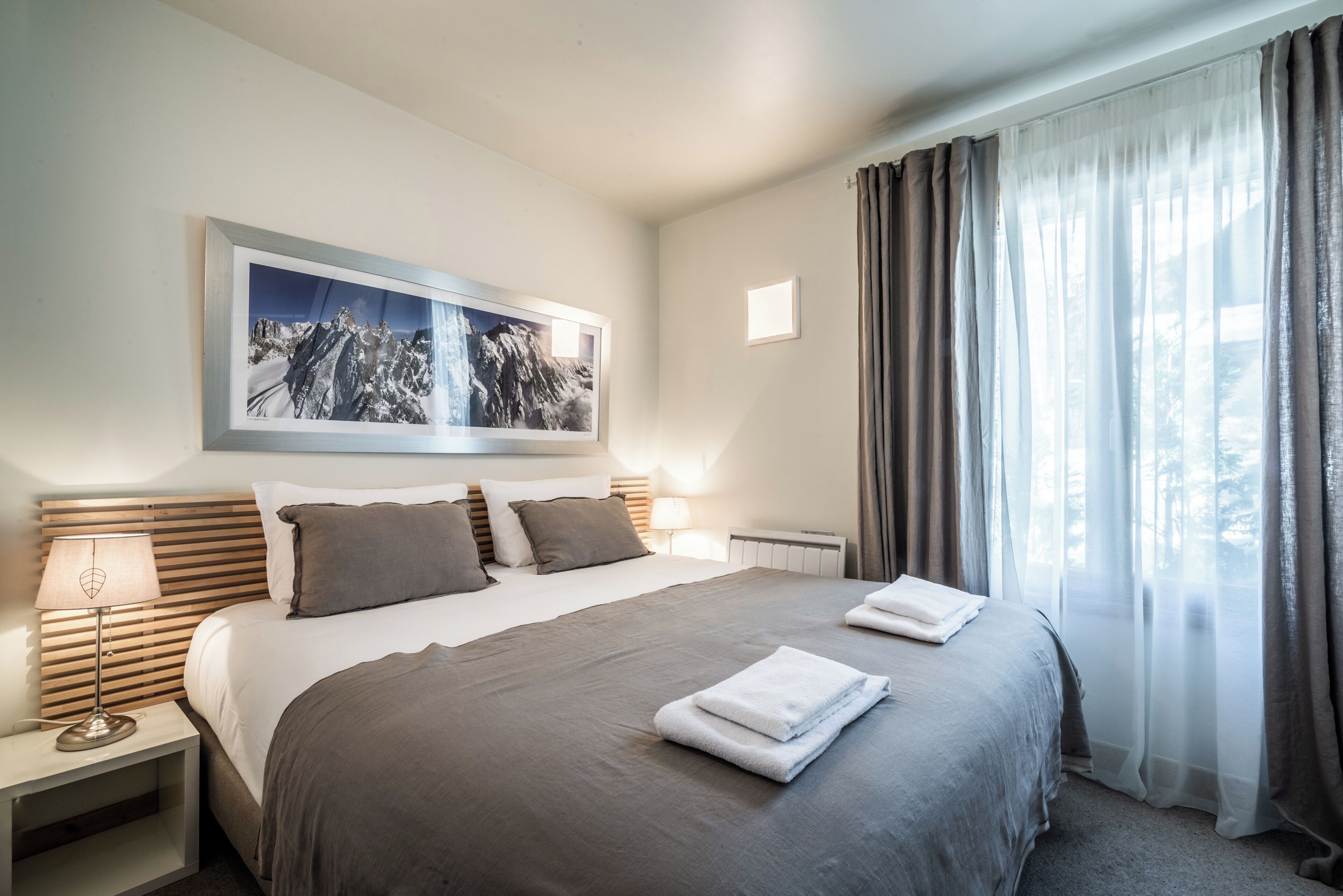 Ein Hotelzimmer mit einem großen Bett, einem Nachttisch mit Lampe, einem gerahmten Bild an der Wand und einem Fenster mit Vorhängen.