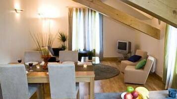 Un comedor con una mesa y sillas de madera, un televisor y un sofá con cojines.