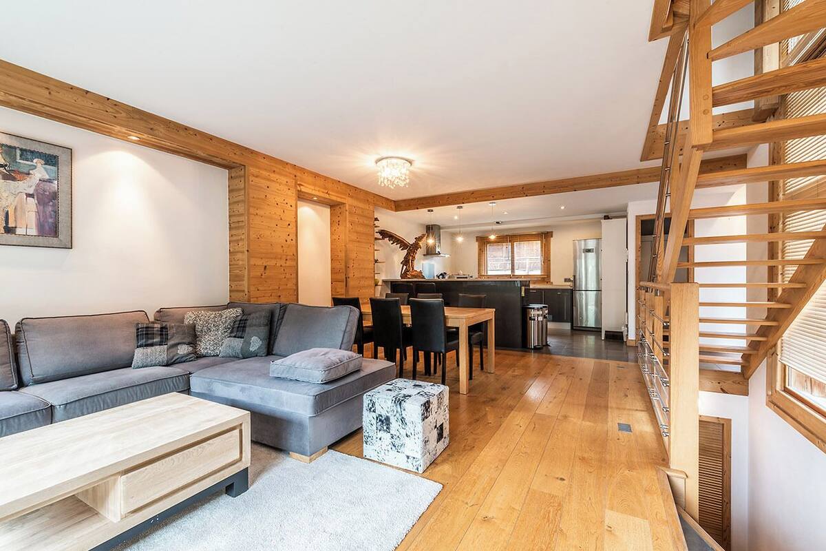 Uma sala de estar moderna com um sofá cinza, piso de madeira e uma escada.