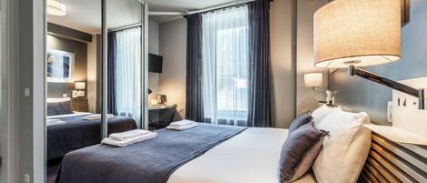 A modern hotel room with a large bed, a desk, a chair, a flat-screen TV, and a large mirror.