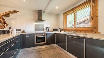 A modern kitchen with dark cabinetry, a built-in oven, a microwave, and a wooden window with blinds.