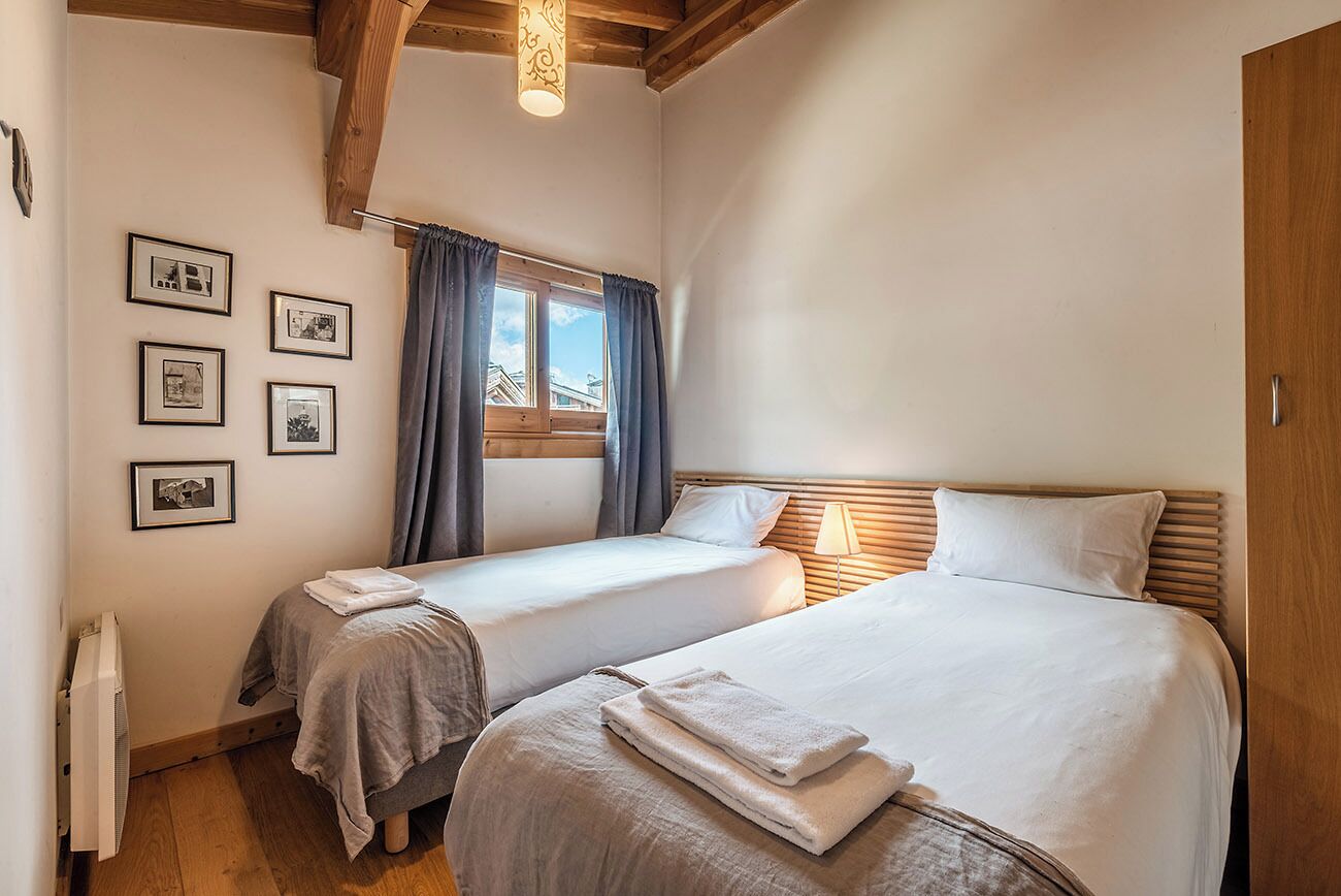 A bedroom with two beds, a window with curtains, and framed pictures on the wall.