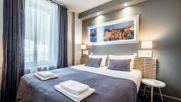 A hotel room with a large bed, a small bedside table, a wall-mounted picture, and a window with curtains.