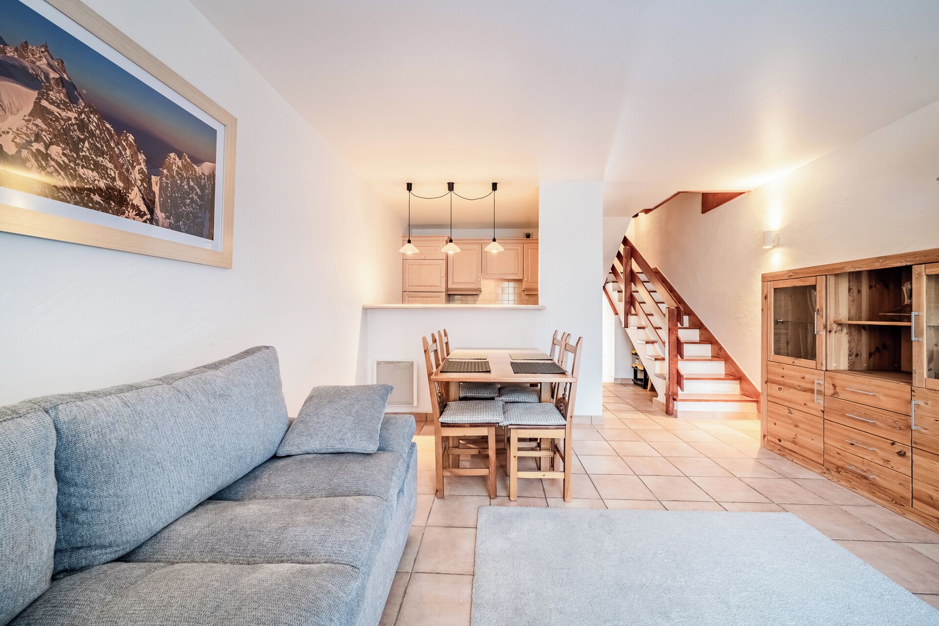 Una sala de estar moderna con sofá, mesa de comedor y sillas. Una escalera conduce a un armario de madera.