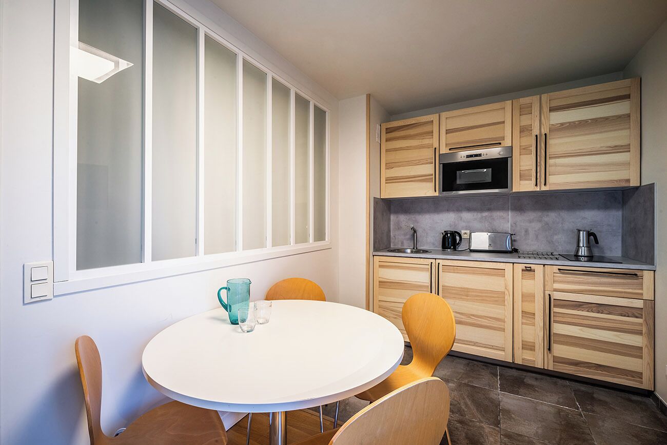 A modern kitchen with wooden cabinets, a stainless steel oven, and a white dining table with chairs.