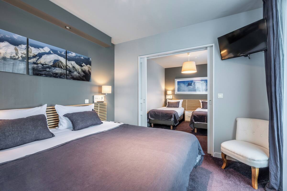 Quarto de hotel com uma cama grande, uma cadeira, uma televisão e um quadro na parede.
