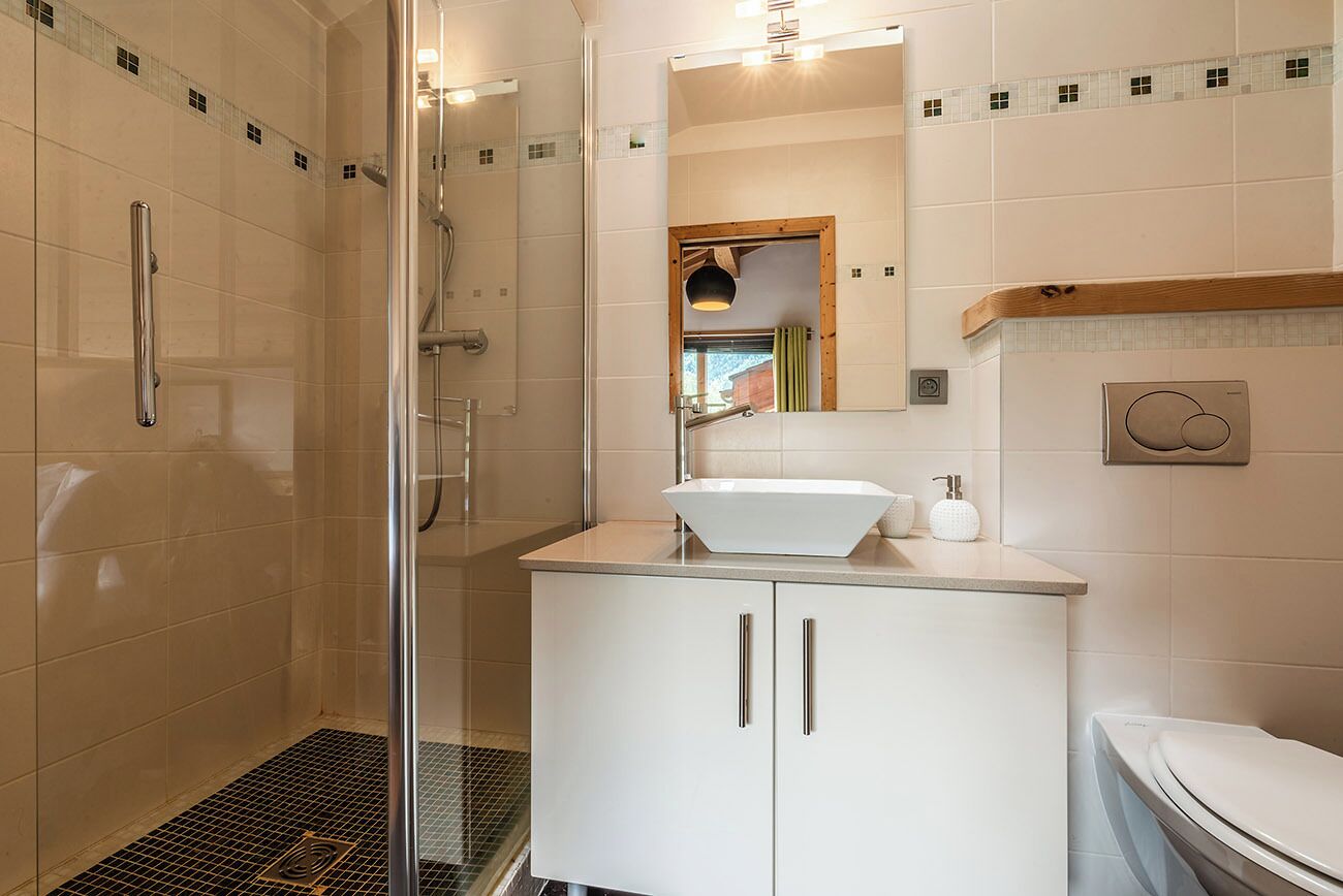 Un baño moderno con cabina de ducha de vidrio, un lavabo blanco y un inodoro.