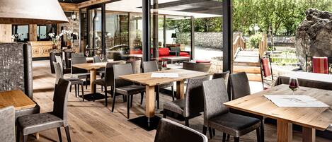 L’intérieur d’un restaurant avec des tables et des chaises en bois, de grandes fenêtres et un mur en pierre.