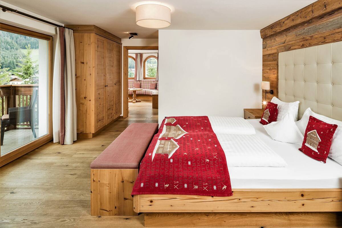 A bedroom with a large bed, wooden floor, and a view of a deck and outdoor area.
