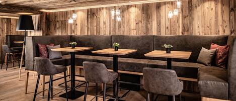 A cozy seating area with a wooden wall, cushioned benches, and tables with potted plants.