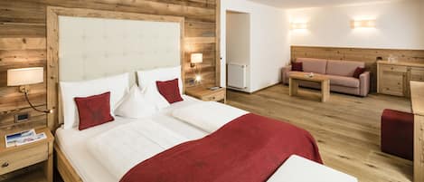 Ein Hotelzimmer mit einem großen Bett, einem Holz-Kopfteil, Nachttischen mit Lampen, einer Holzkommode, einem kleinen Tisch und einem Sofa.