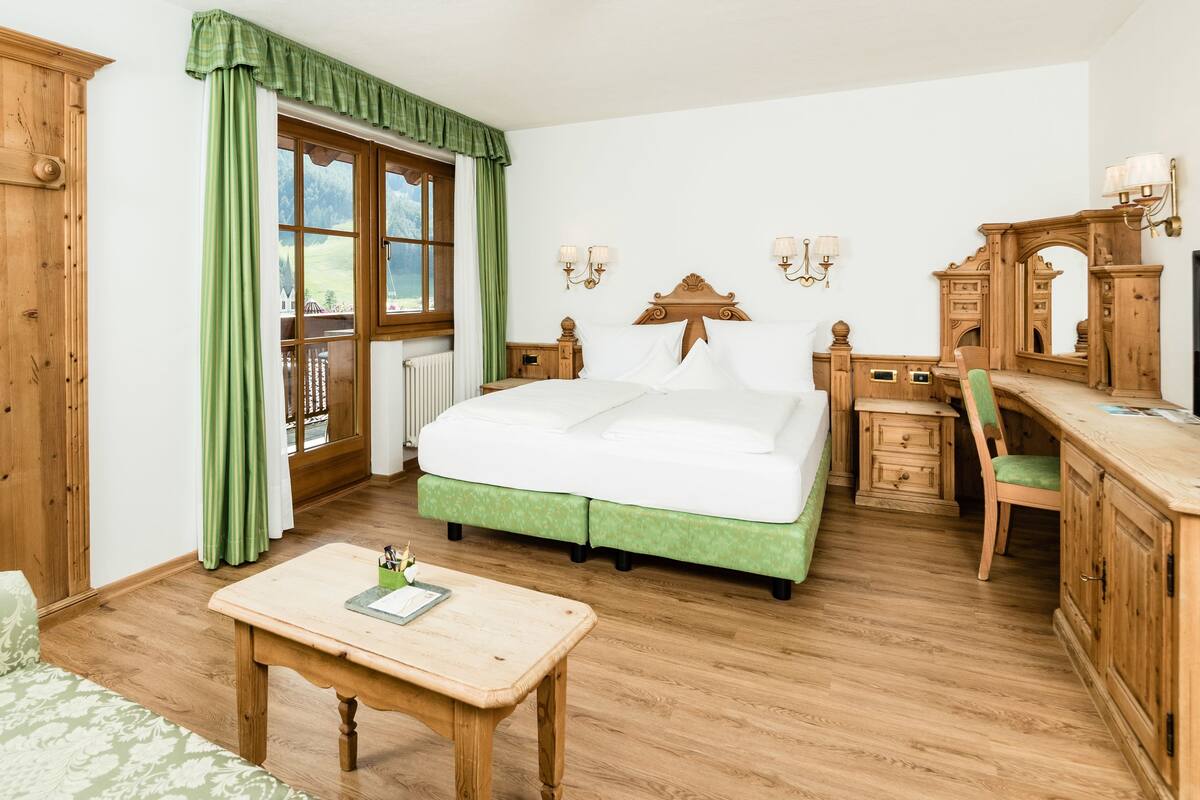 A bedroom with a bed, bedside tables, a desk, a chair, a television, and a window with curtains.