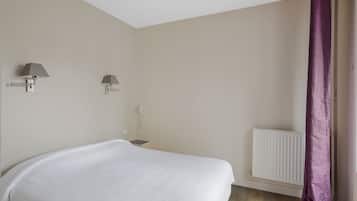 Un dormitorio con una cama, dos lámparas fijadas a la pared, un radiador blanco y una cortina morada.