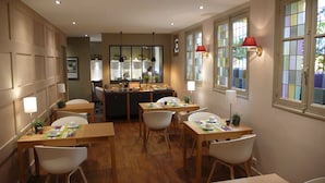 A dining area with wooden tables and white chairs, a central island with kitchen appliances, and windows with red lamps.