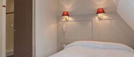 Una habitación de hotel con una cama, un teléfono y dos lámparas fijadas a la pared.