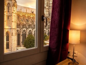 Een raam met uitzicht op een historisch gebouw met ingewikkelde architectuur, een deur en een lamp op een nachtkastje.