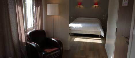 A hotel room with a bed, a chair, a lamp, and a door.
